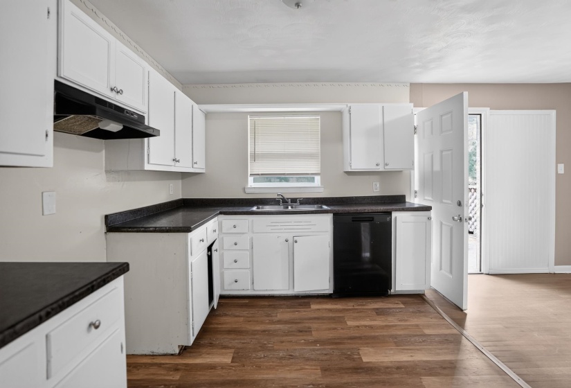Kitchen featuring white cabinetry, dark countertops, a stainless steel sink, a black dishwasher, and wood-finish flooring