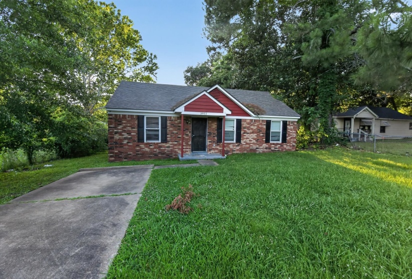 Brick facade home featuring a red-accented gable, black shutters, and a gray shingled roof