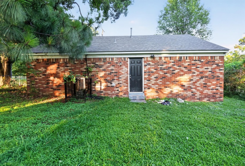 Brick exterior featuring a black entry door with transom window, concrete steps, and a dark shingle roof