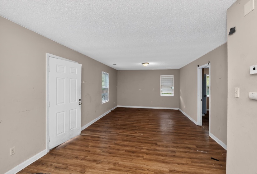 Spacious interior room featuring wood-finish flooring, neutral wall tones, white trim, and multiple windows