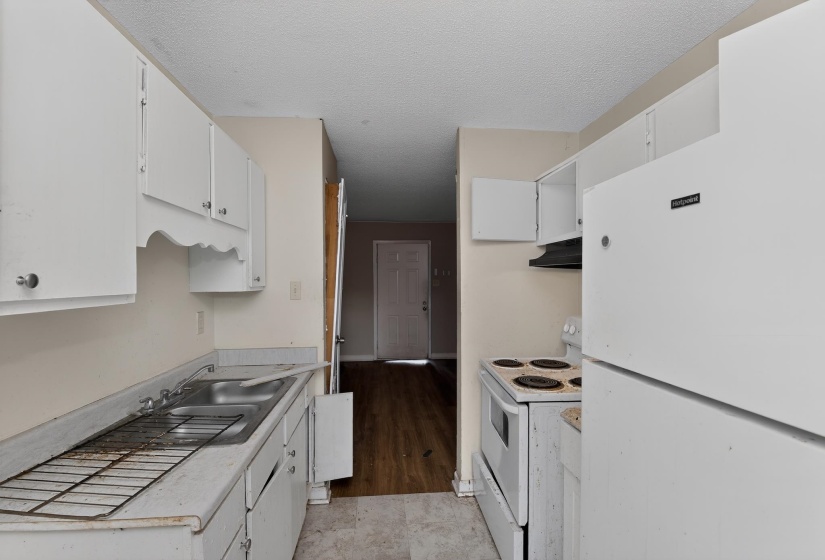 Compact kitchen featuring white cabinetry, a double basin stainless steel sink, a refrigerator, and an electric range