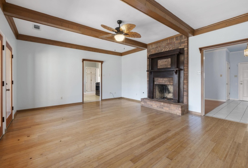 Unfurnished living room featuring light wood-style flooring, ceiling fan, a fireplace, beamed ceiling, and crown molding