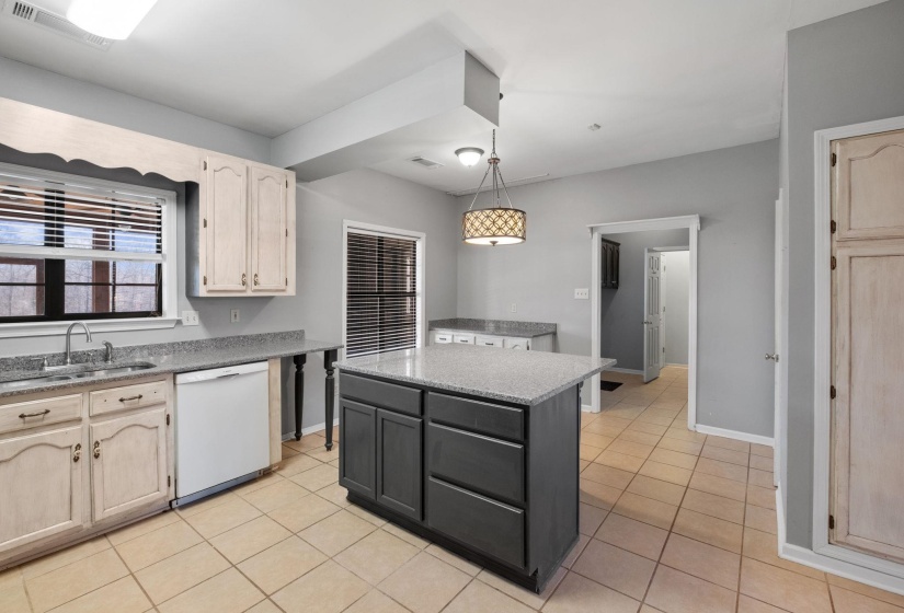 Kitchen featuring a center island, dishwasher, pendant lighting, light stone countertops, and light tile patterned floors