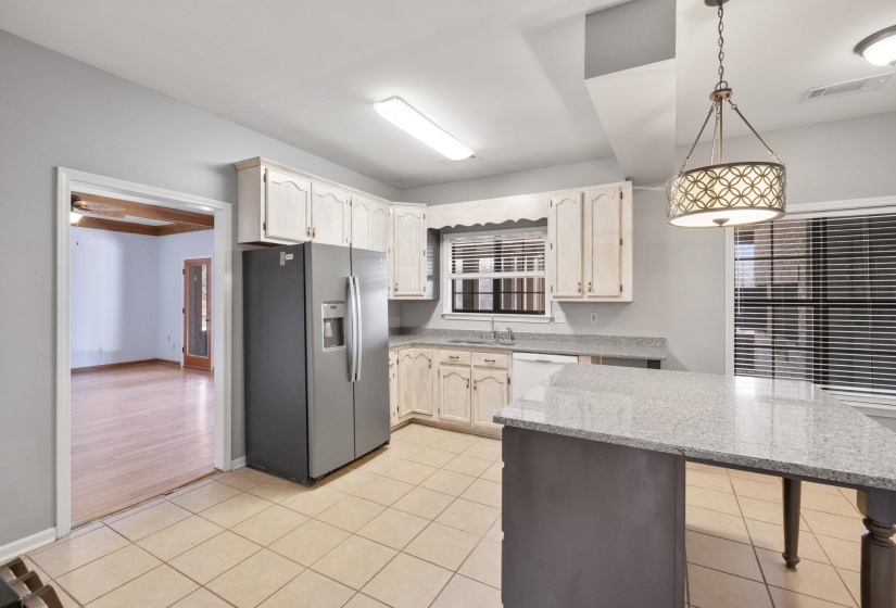 Kitchen featuring stainless steel refrigerator with ice dispenser, hanging light fixtures, light stone countertops, a breakfast bar area, and light tile patterned floors