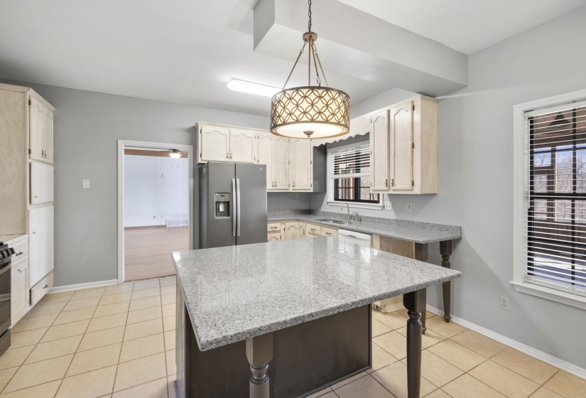 Kitchen with stainless steel fridge, pendant lighting, light stone countertops, light tile patterned flooring, and a center island