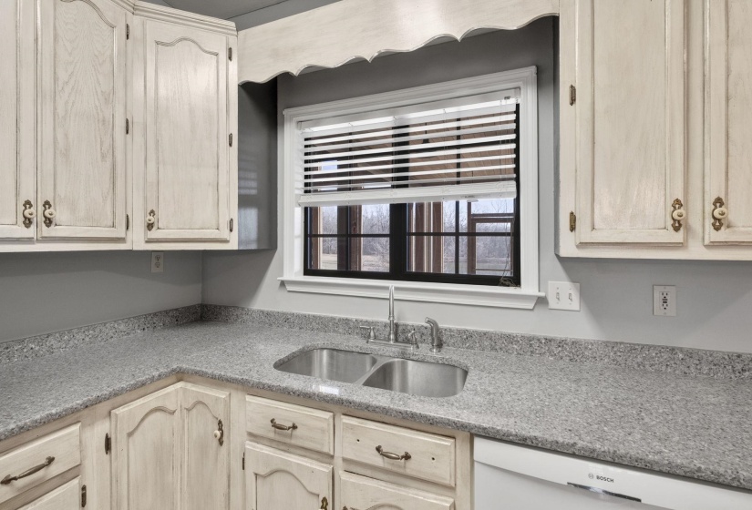 Kitchen featuring white dishwasher, light stone countertops, and light brown cabinetry