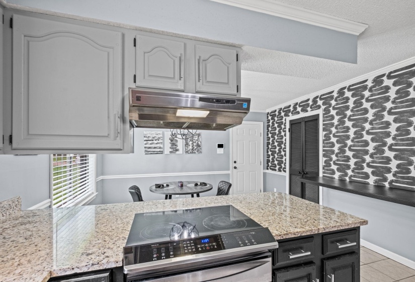Kitchen featuring an island with a built-in cooktop, light-toned countertops, gray upper cabinetry, dark lower cabinetry, and a stainless steel range hood