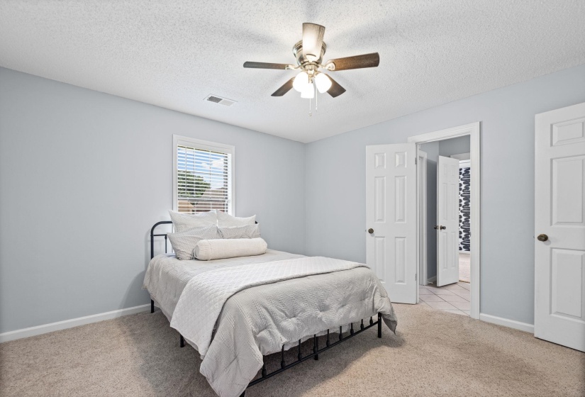 Bedroom featuring light-toned walls, textured carpet flooring, and a ceiling fan with integrated lighting