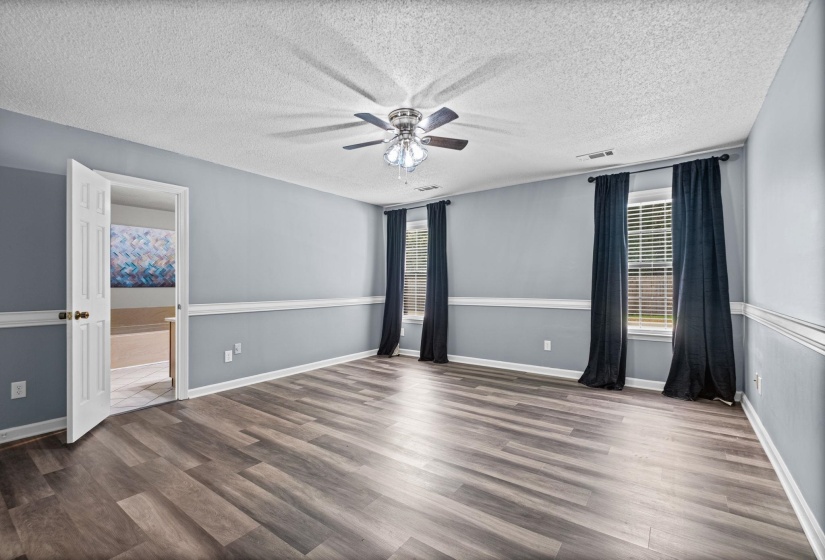 Spacious room featuring wood-finish flooring, light blue walls with chair rail molding, and a ceiling fan with integrated lighting