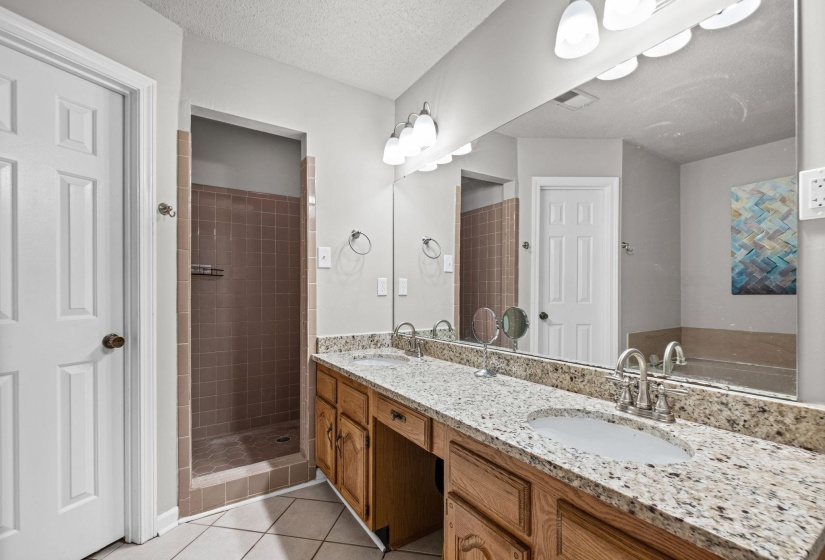 Bathroom featuring a double vanity with stone countertops, integrated sinks, a built-in shower stall with tile surround, and a drop-in tub