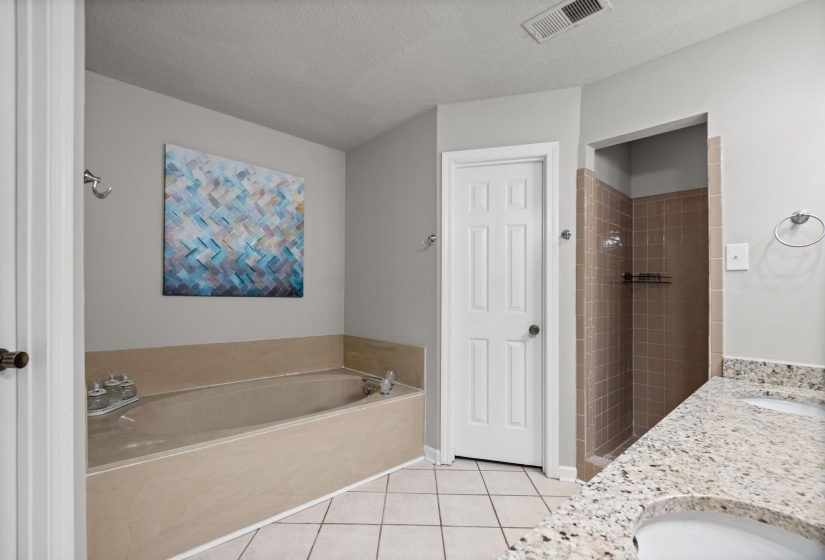 Bathroom featuring a built-in tub, tiled shower enclosure, and a double vanity with stone-finish countertops and integrated sinks