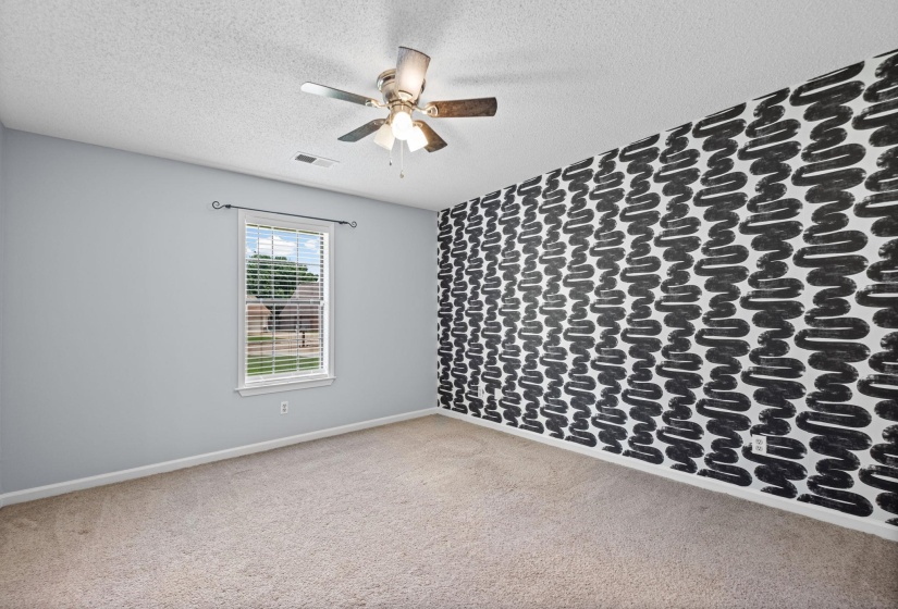 Spacious room featuring a neutral carpet, a window with blinds, and a decorative accent wall