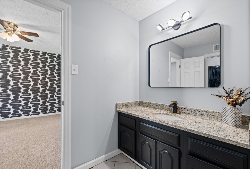 Bathroom vanity featuring a speckled countertop, black cabinetry, and a black-framed rectangular mirror