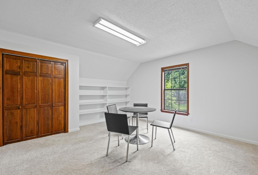 Carpeted room with a multi-pane window, built-in shelving, wood-paneled bi-fold closet doors, and recessed fluorescent lighting