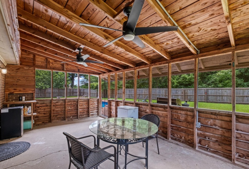 Screened patio featuring a wood-paneled ceiling and walls, concrete flooring, and multiple ceiling fans