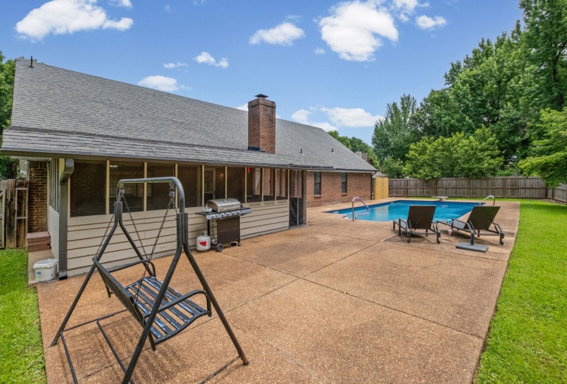 Expansive concrete patio featuring a rectangular swimming pool with surrounding grass, a wood privacy fence, and a screened-in porch with horizontal siding