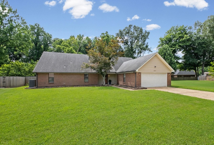 Brick exterior home featuring a two-car garage, mature landscaping, and a substantial front lawn