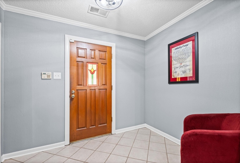 Wood-paneled front entry door featuring a stained glass insert, tile flooring, light gray walls, white crown molding, and a flush-mount ceiling light fixture