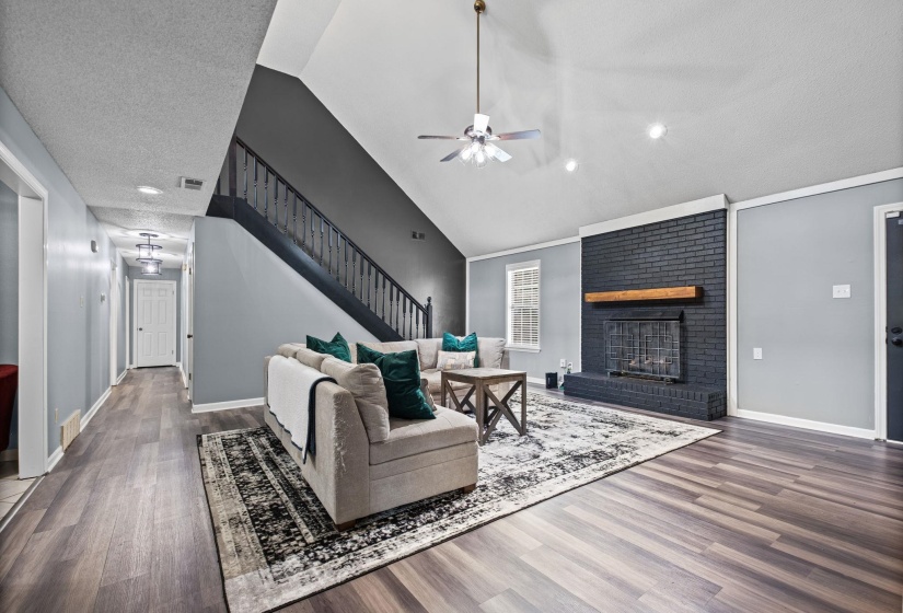 Spacious living area featuring high vaulted ceilings, wood-finish flooring, and a painted brick fireplace with a wood mantle
