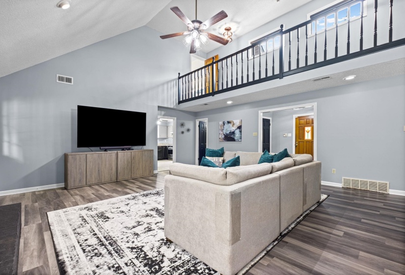 Open-concept living space featuring vaulted ceilings, dark wood-finish flooring, and a second-story interior balcony with black spindle railing