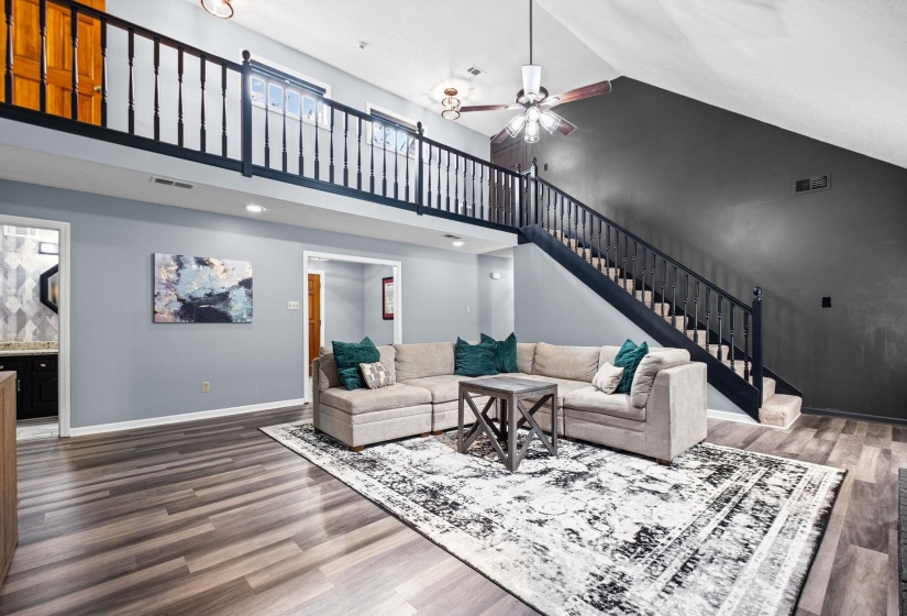 Vaulted ceiling living area featuring wood-finish flooring, an open loft with a black baluster railing, and a coordinating black baluster staircase