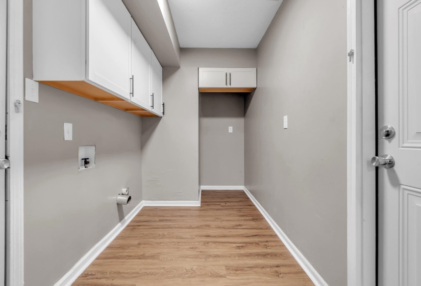 Laundry area featuring white cabinetry with dark hardware, wood-finish flooring, and light gray wall paint