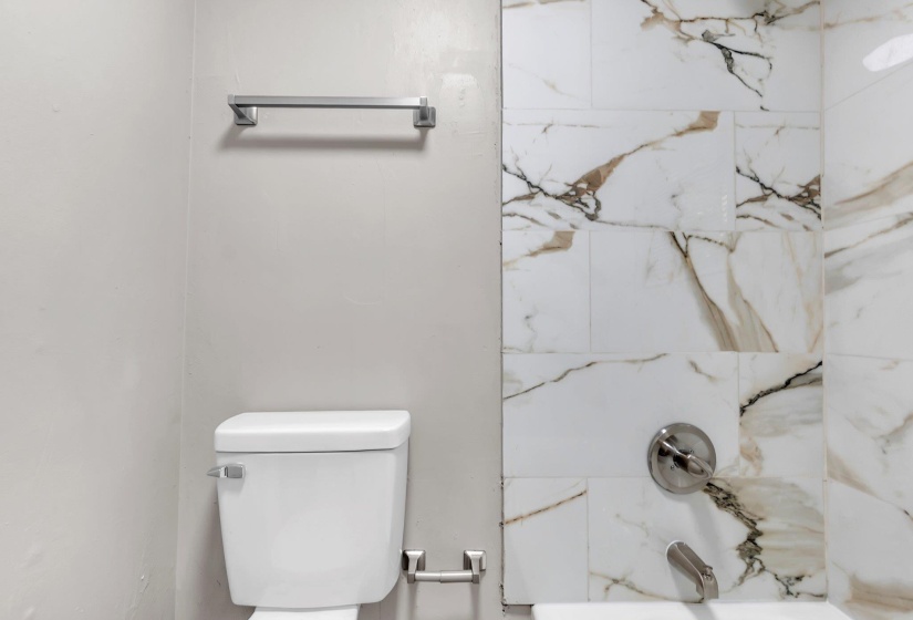 Bathroom featuring a white toilet, chrome towel bar, and a tiled shower/tub combination with white and brown veined tiles