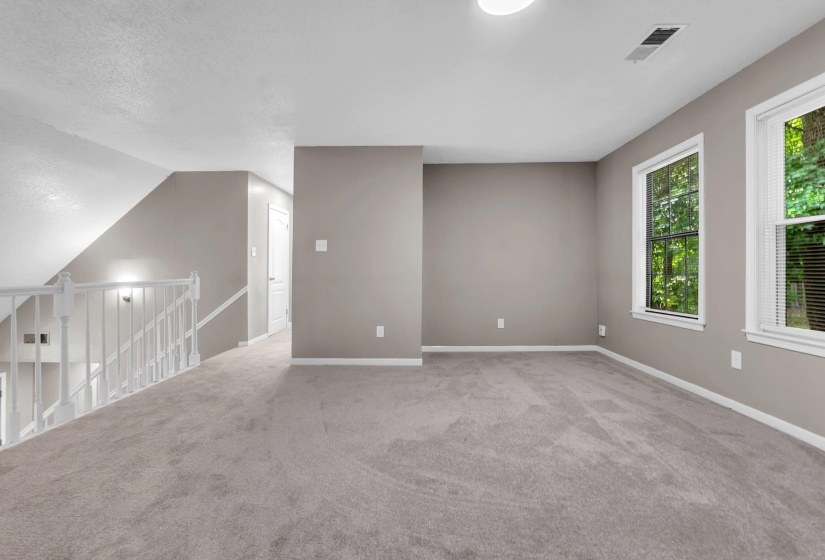 Spacious carpeted room featuring multiple windows, neutral wall tones, white trim, and a white baluster railing