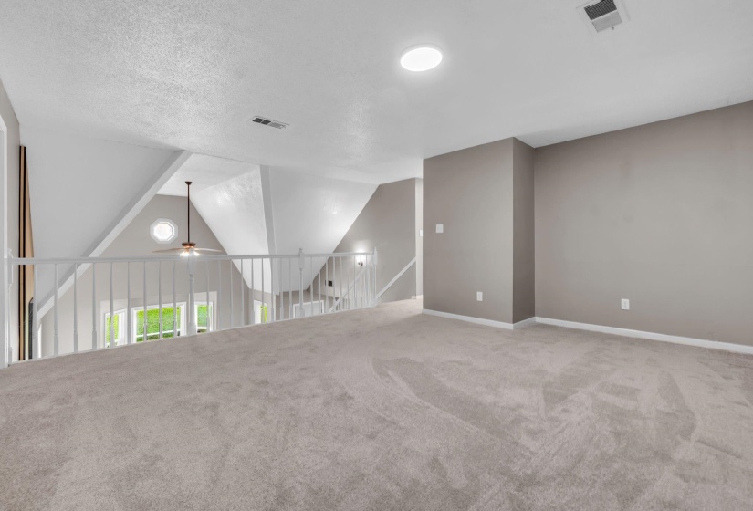 Spacious loft area featuring light gray carpet flooring, neutral painted walls, and a recessed ceiling light