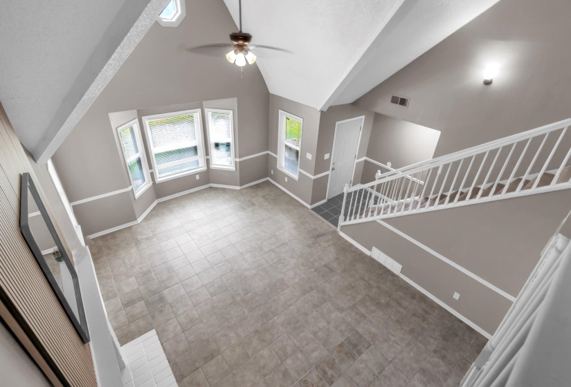 Expansive living area featuring vaulted ceilings, bay windows, ceiling fan, and tile flooring