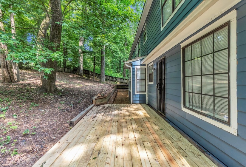 Expansive wood deck extending alongside the property, offering direct access to the exterior via a sliding glass door with a security gate