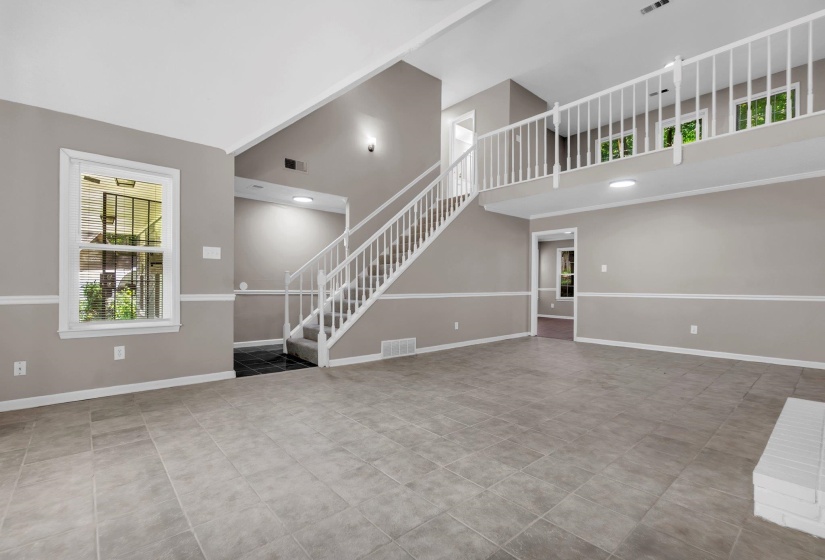 Spacious living area featuring large format tile flooring, a prominent staircase with white banister, and a second-story interior balcony