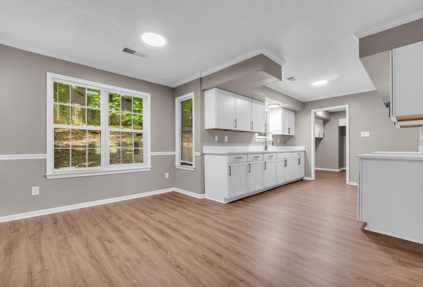 Open-concept living area featuring wood-finish flooring, a kitchen with white cabinetry and light-colored countertops, and multiple windows