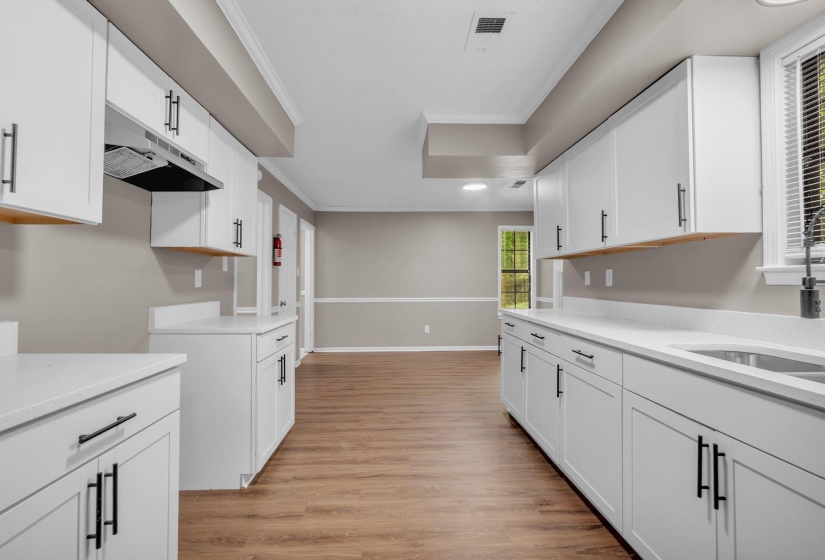Contemporary kitchen featuring white cabinetry with matte black hardware, white countertops, stainless steel sink with a matte black faucet, and wood-finish flooring