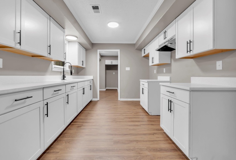 Galley kitchen featuring wood-finish flooring, white cabinetry with black hardware, white countertops, and a black gooseneck faucet