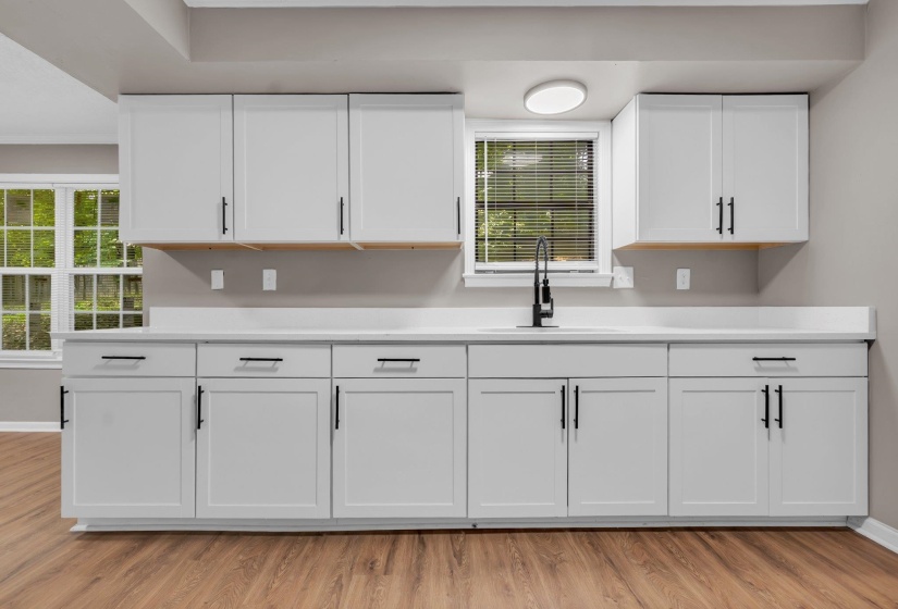 Updated kitchen featuring white shaker cabinetry, black hardware, a window with blinds, and wood-finish flooring