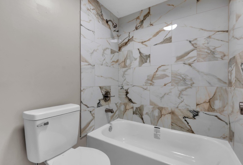 Bathroom featuring a white porcelain toilet, a white soaking tub, and floor-to-ceiling marble-look wall tiling