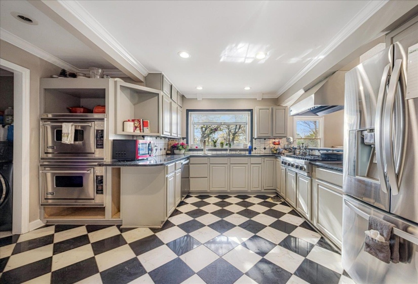Kitchen featuring stainless steel appliances, dark stone counters, ornamental molding, wall chimney range hood, and open shelves