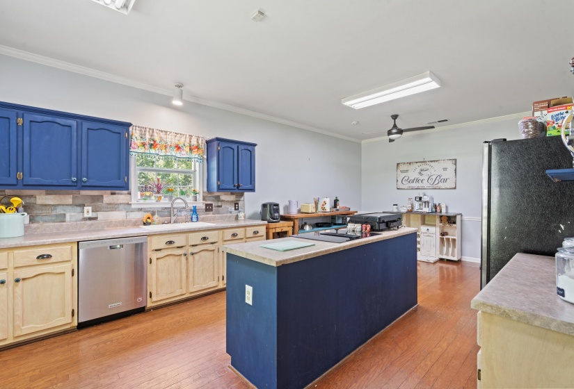 Kitchen featuring a central island, wood-finish flooring, a stainless steel dishwasher, and a window above the sink