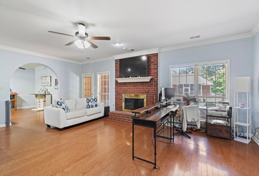Expansive living area featuring wood-finish flooring, a brick fireplace with a mantel, and an arched doorway leading to an additional space