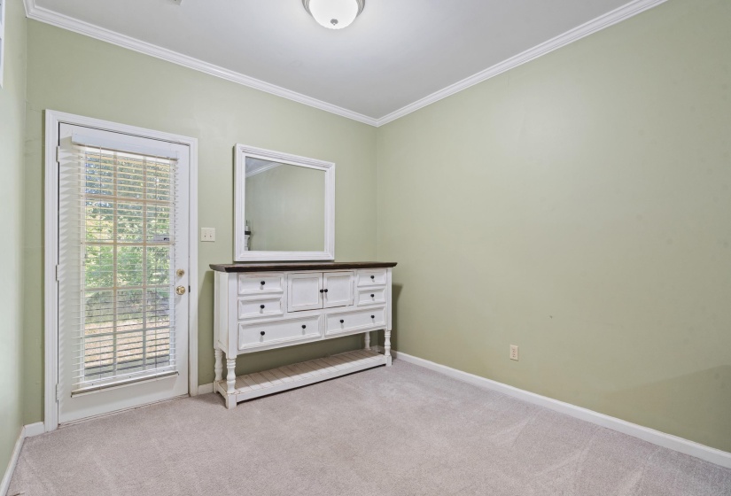 Room featuring a glass-paneled door with integrated blinds, crown molding, light-colored walls, and neutral carpet flooring