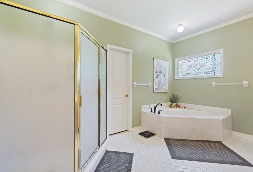 Bathroom featuring a corner soaking tub with a black faucet, a framed privacy window with a decorative pattern, and a shower enclosure with gold-tone framing and frosted glass panels