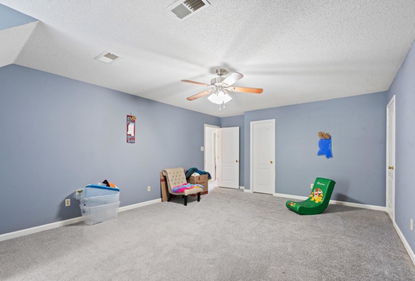 Spacious room featuring light blue walls, gray carpet, multiple white doors, a ceiling fan with integrated lighting, and white trim