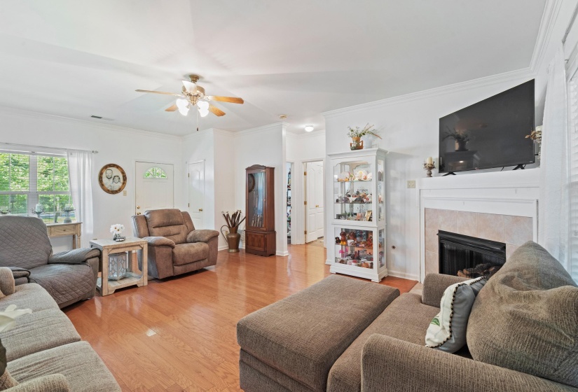 Spacious living area featuring wood-finish flooring, a ceiling fan, and a fireplace with a white mantel and tile surround