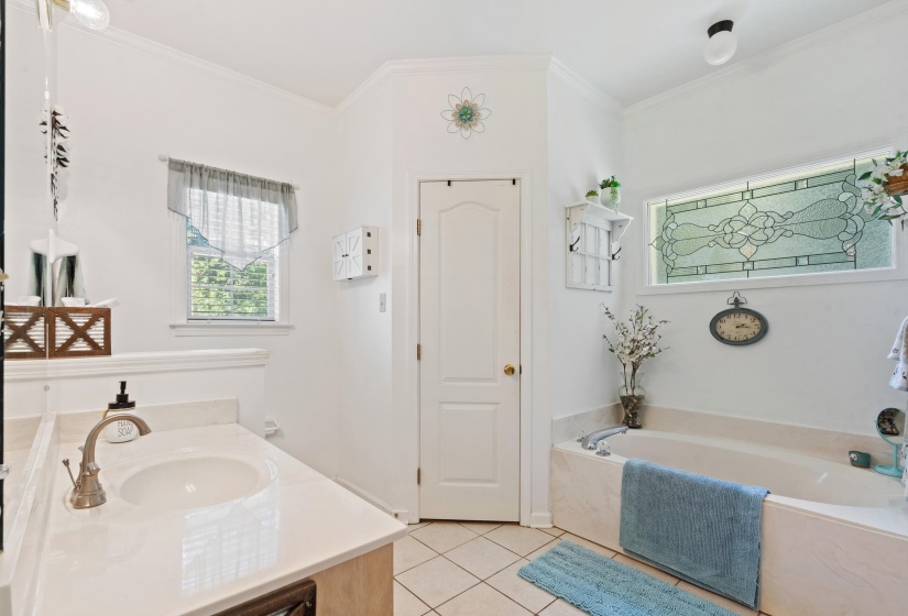 Bathroom featuring a built-in tub with tile surround, a single vanity with an integrated sink and light-toned countertop, and tile flooring