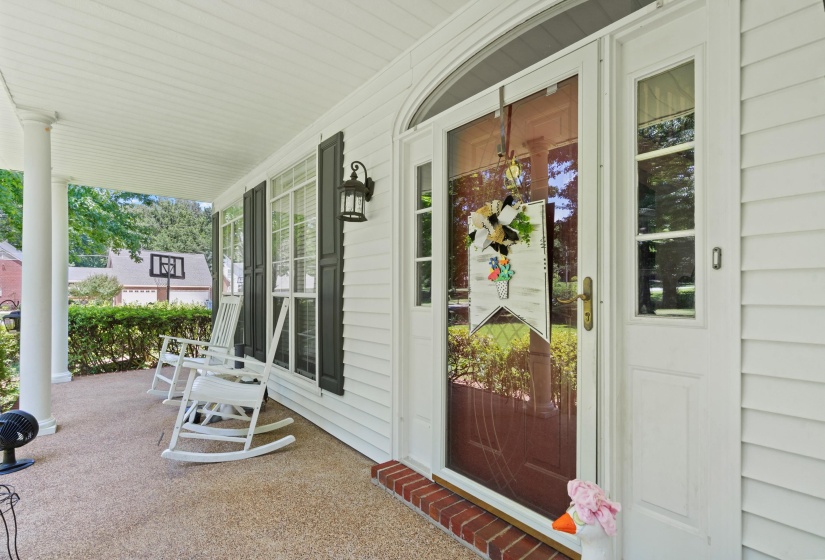 Inviting front porch featuring white siding, dark louvered shutters, a decorative wall-mounted lantern, and a secure glass storm door