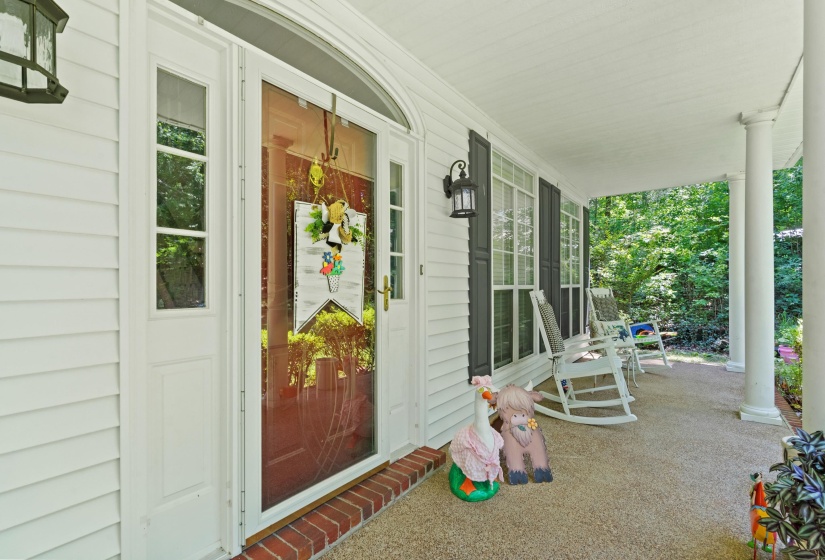 Inviting covered front porch featuring white siding, a red brick base, white columns, and dark window shutters