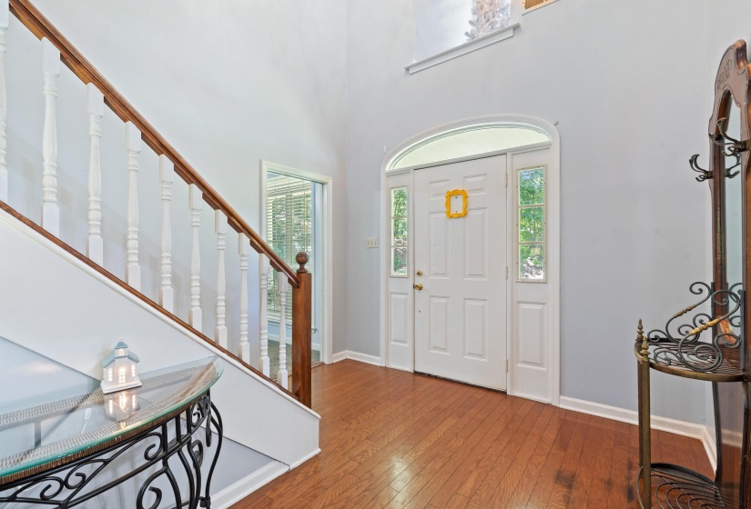 Two-story foyer featuring wood-finish flooring, a grand staircase with white spindles and wood handrail, an arched transom window, and a paneled entry door with sidelights