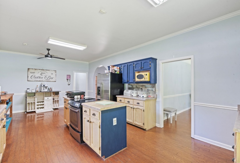 Spacious kitchen featuring wood-finish flooring, a central island with integrated range, contrasting cabinetry, a built-in refrigerator, and an arched doorway