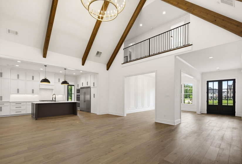 Spacious open-concept interior featuring vaulted ceilings with exposed wood beams, a prominent kitchen island with a white countertop, extensive white cabinetry, and wood-finish flooring
